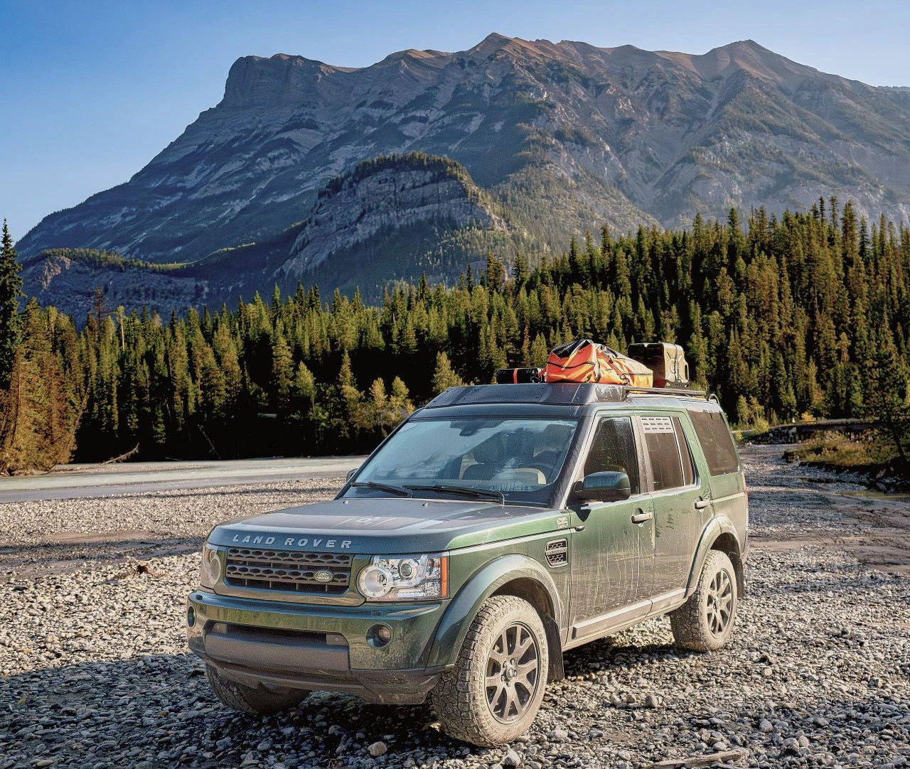 Green Land Rover SUV with roof rack in mountainous forest landscape